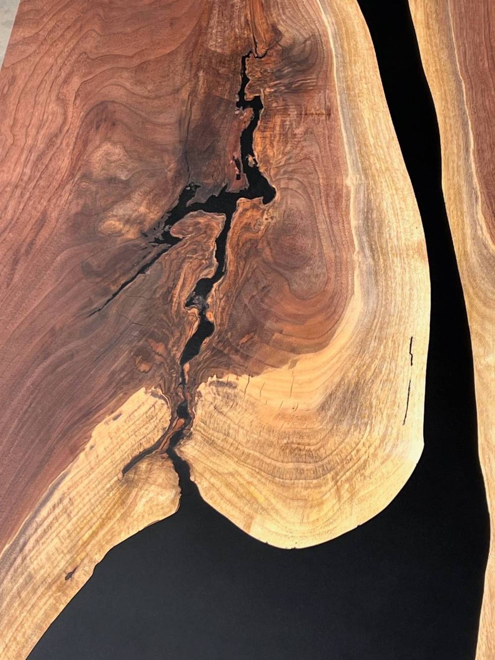 Close detail of a black walnut slab, sapwood meeting dark heartwood with a natural void filled in black epoxy