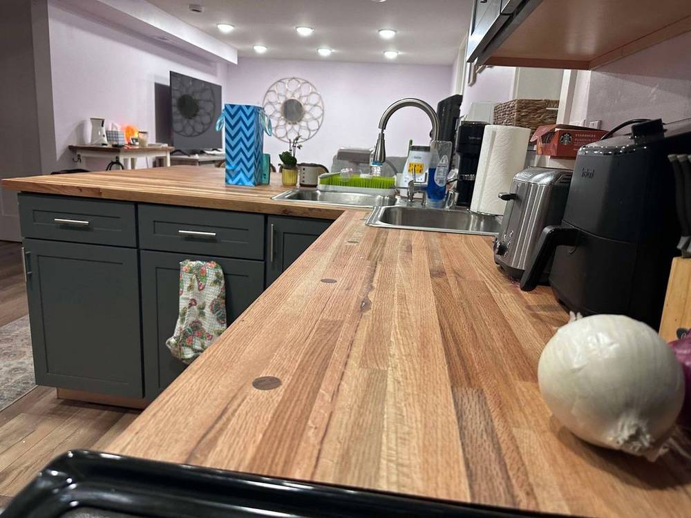 Kitchen with a reclaimed butcher block countertop run along dark green cabinets