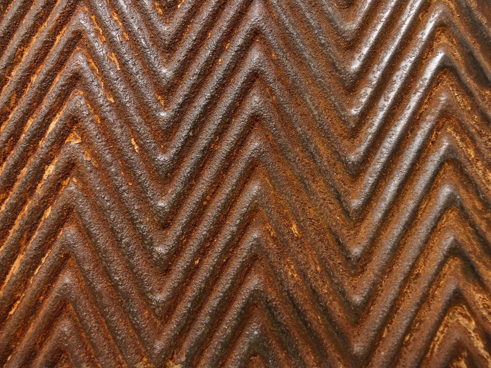 Close view of a coal-fired steel sheet, the chevron corrugation running across rust and pale calcium banding