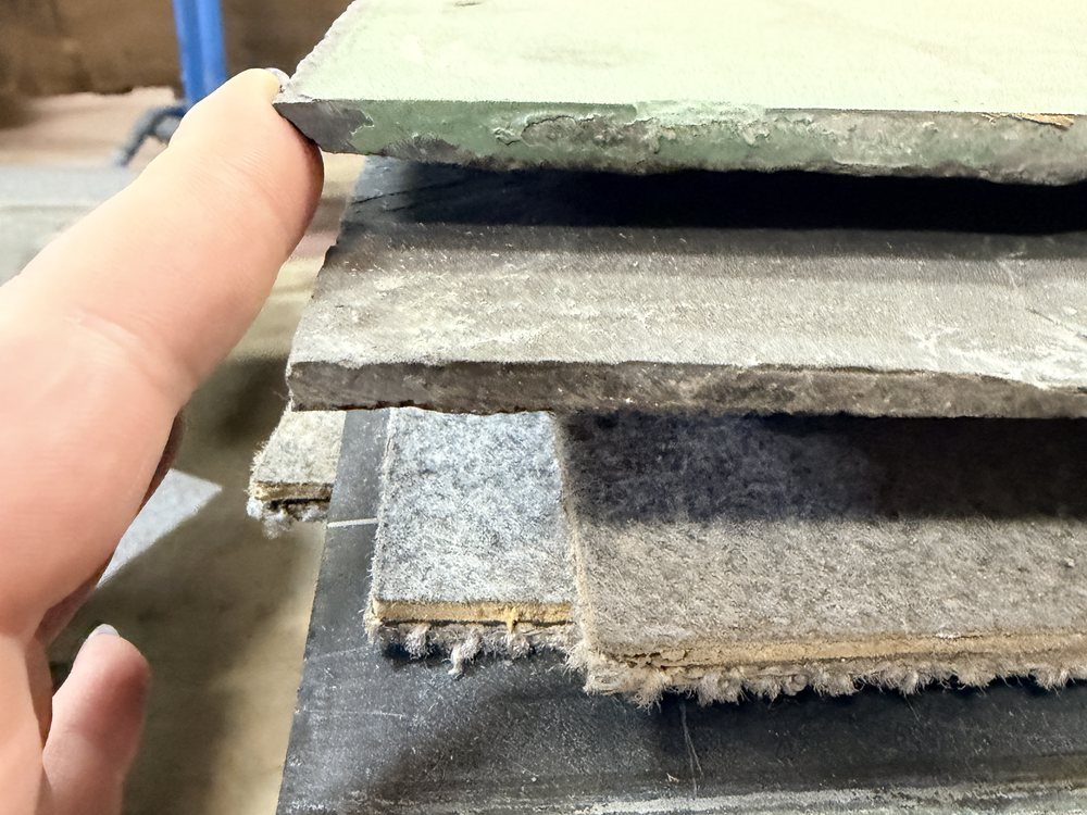 Hand lifting the corner of a slate chalkboard piece, showing the thickness and the layered stack beneath