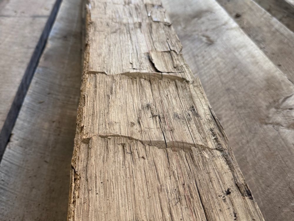 Hand-hewn barn beam laid out in the yard, axe scallops running the full length of the face