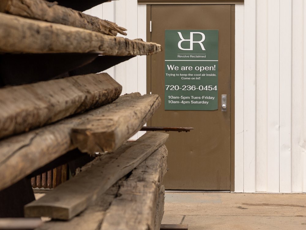 Stacked hand-hewn beams beside the Revolve Reclaimed sign at the yard entrance