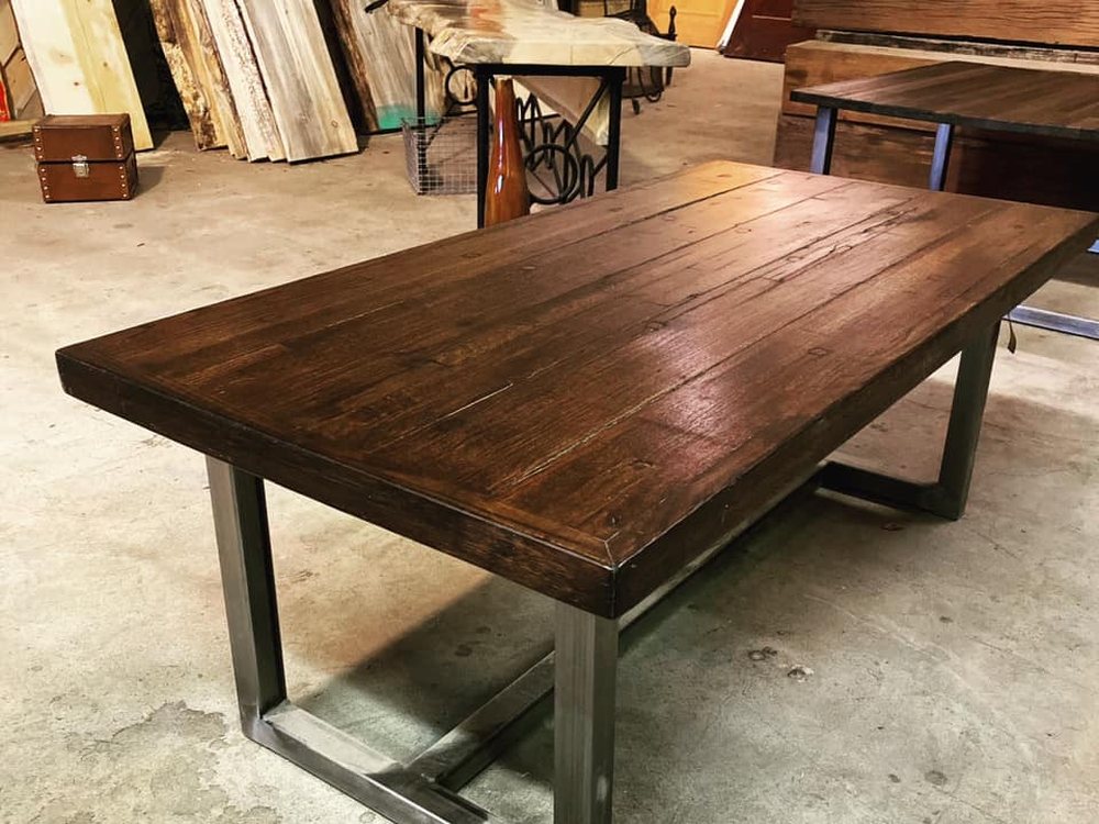 Dark plank table top on a rectangular steel base in the yard, the frame visible under the full length of the table