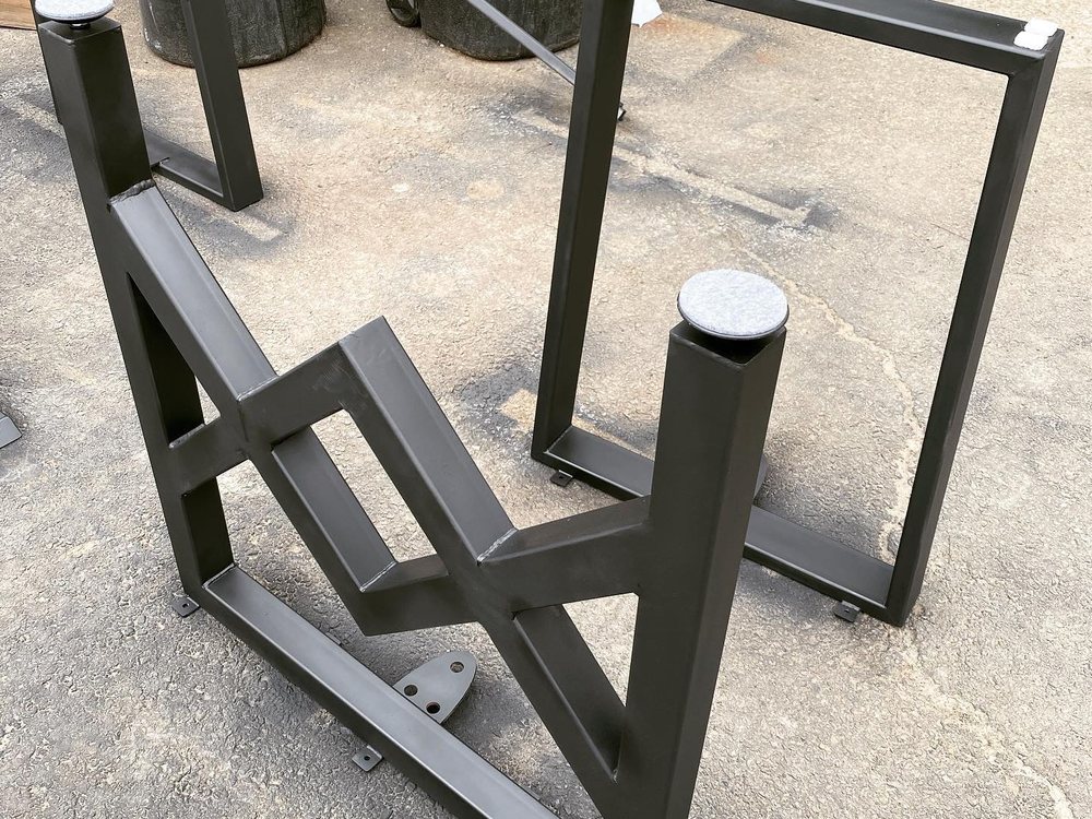 Bare steel table base upside down on the shop floor, welded bracing and levelling feet visible