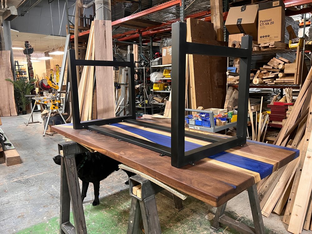 Steel base being fitted upside down onto a river table top on sawhorses in the Denver shop