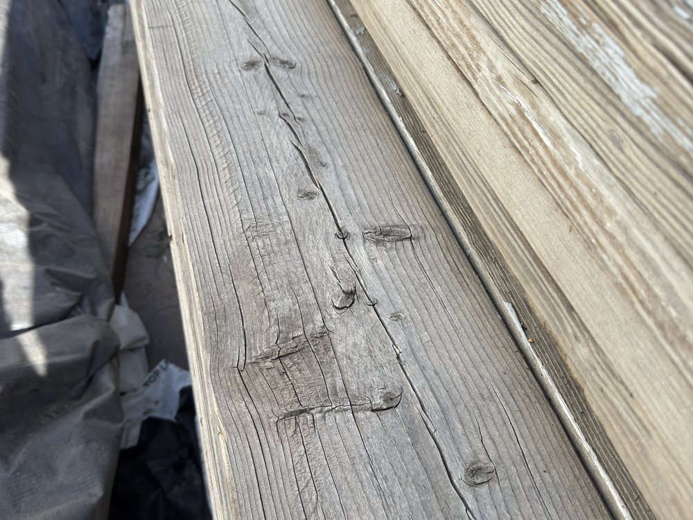 Worn seating face of a speedway bleacher plank in raking light, silvered Douglas fir with tight grain and old checks