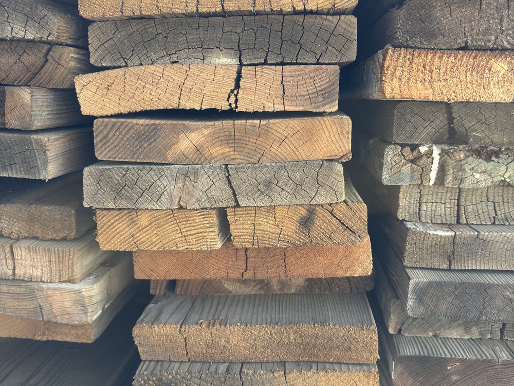 Stack of speedway bleacher fir seen end on, weathered grey faces above fresh orange sawn ends